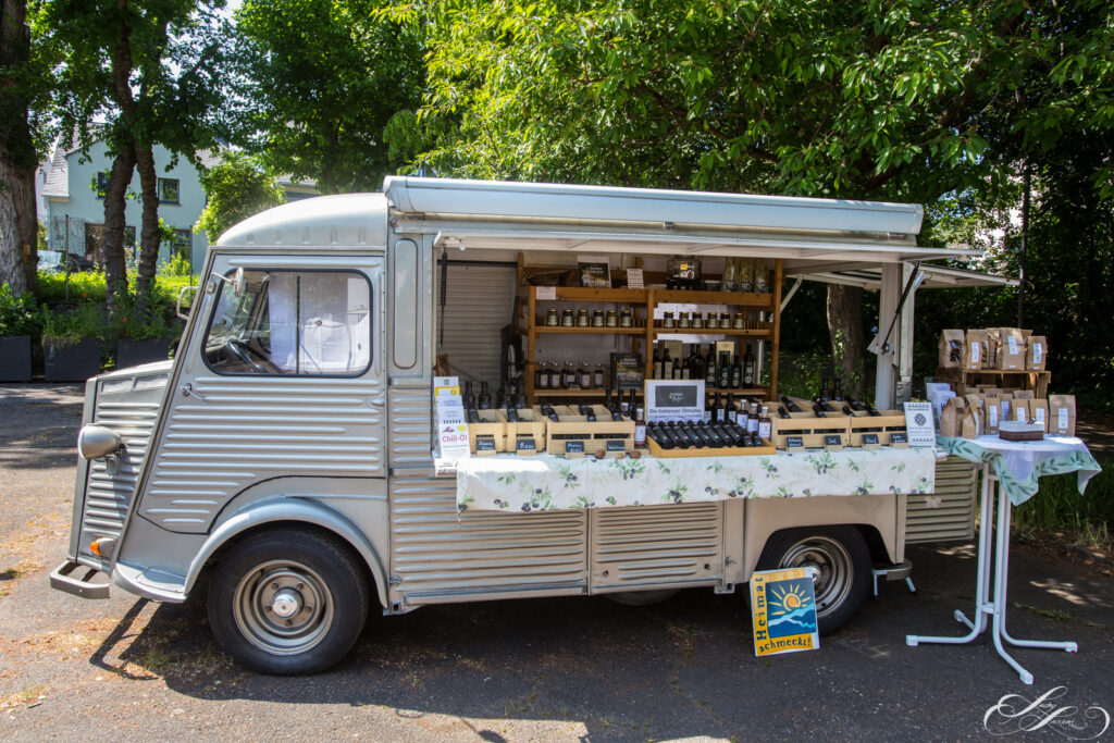 Ein alter Foodtruck, der in einem sonnigen Bereich im Freien geparkt ist, stellt Gläser, Flaschen und verpackte Lebensmittel auf Regalen und einem Tisch aus - perfekt, um die DANKE-Spezialitäten von 2023 zu entdecken.